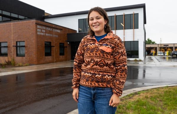 A person poses for a photo outside a school