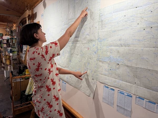 A woman in a red and white dress points to a map hanging on the wall.