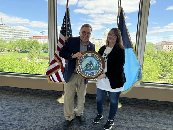 Two people posing for photo with Minnesota state seal