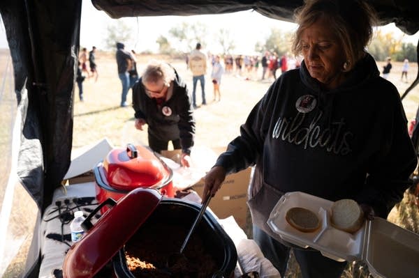 A woman in a sweatshirt scoops food onto a Styrofoam plate.