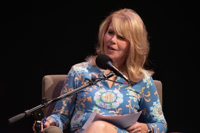 Two people sit on a stage with microphones.