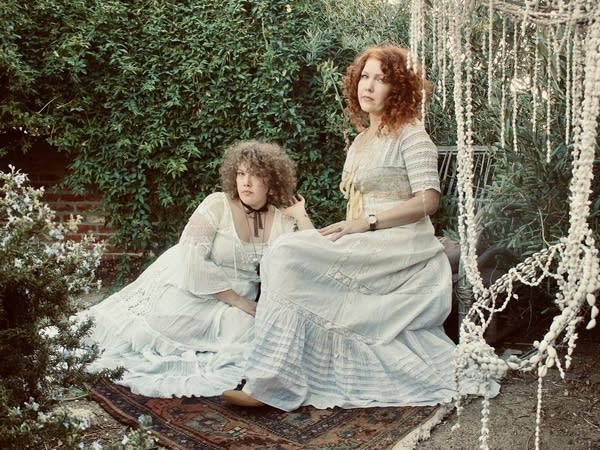 Two women in formal dresses sitting in a lush garden.