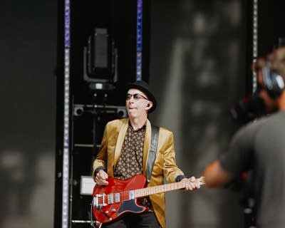 A man in sunglasses and a porkpie hat plays guitar onstage
