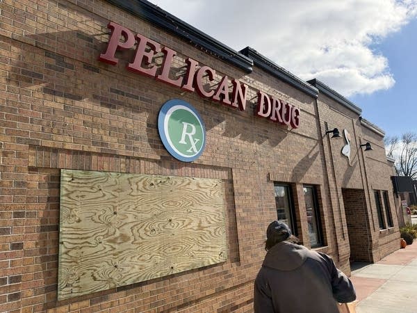 A business with a boarded up window, and a sign that reads "Pelican Drug."