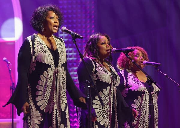 Three musicians sing together onstage