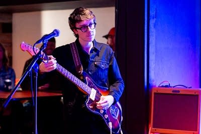 A musician plays guitar onstage in a music venue