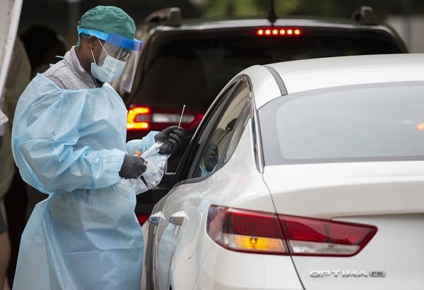 A person wearing personal protective equipment talks to a person in a car.