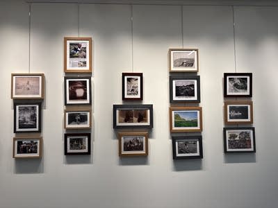 Columns of framed photographs hang on a white wall.
