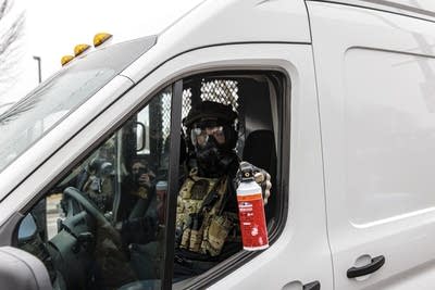 An officer sprays a chemical irritant out the window of a white van.