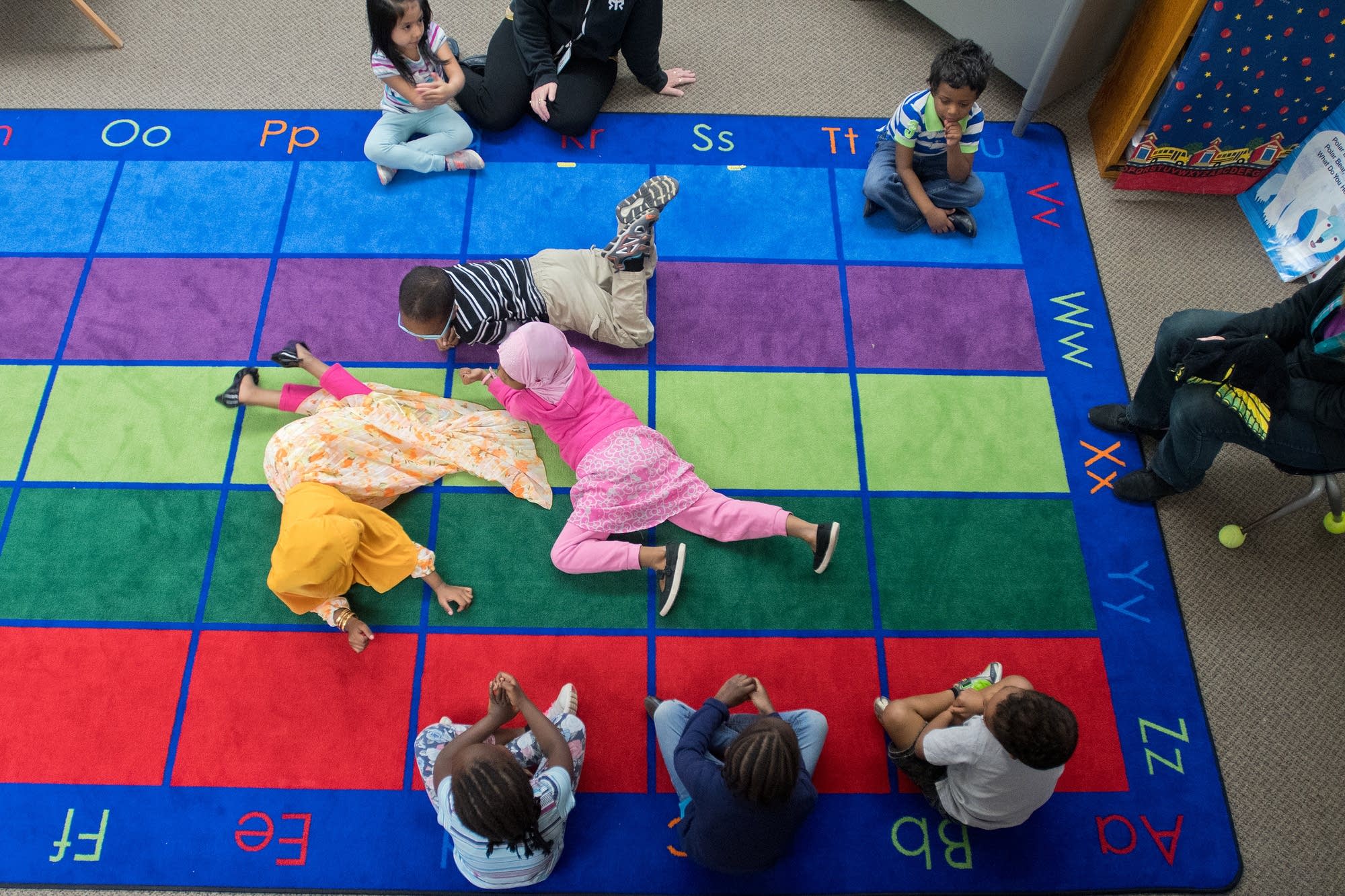 Preschoolers crawl on the carpet as students sing a song about earthworms.