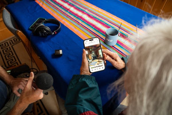 Over-the-shoulder shot of a woman showing photos on her phone to a reporter holding a microphone.