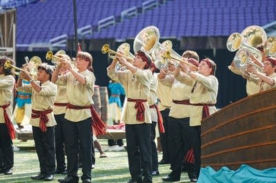 A marching band performs on the field of a football stadium.