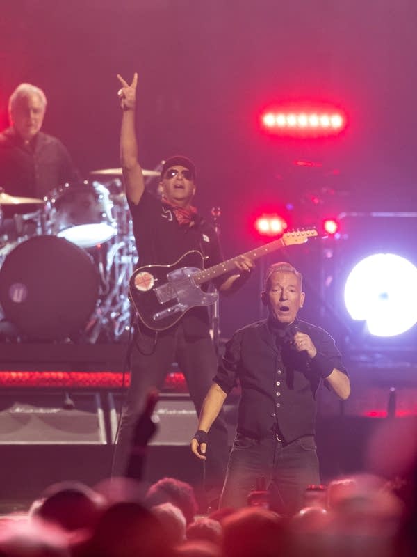 Three musicians performing onstage during an arena concert