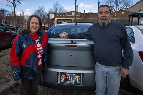 Two people stand next to a car