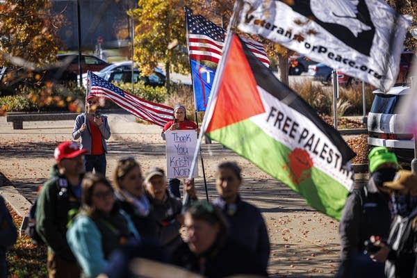 Signs and flags are on display during a protest near a parking lot.