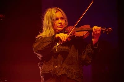 A musician plays violin onstage in a large music venue