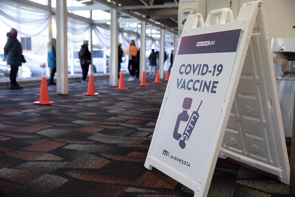 A sign reads covid-19 vaccine near people standing in line. 