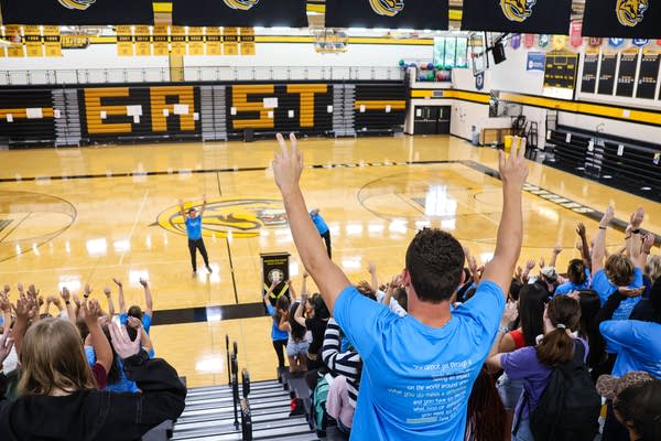 Students raise their arms during an assembly in a gymnasium.