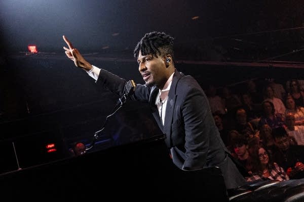 A man sings and plays piano in an auditorium filled with people