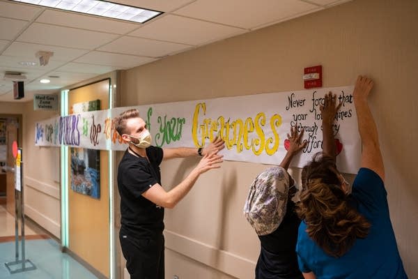 Three people hang a long banner on a wall.