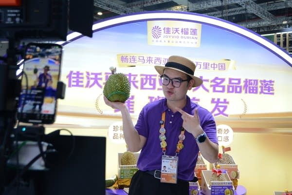 A man holds up a Malaysian durian during a livestream at the 2025 China import expo