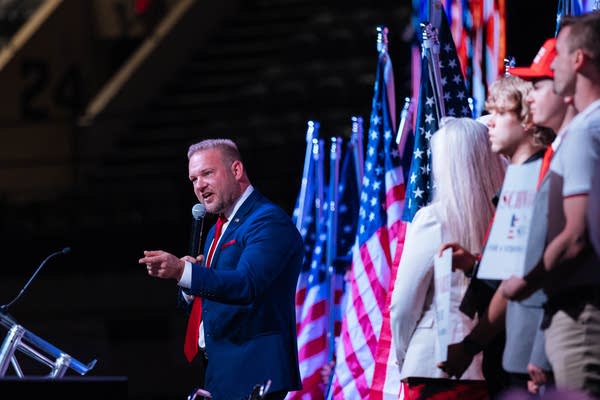 Man in suit talking into a mic with flags in background