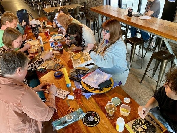 People gather around a wooden table inside a brewery to create crop art.