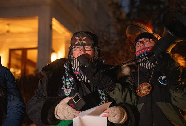 Two speakers bundled up in winter gear talk into a microphone.