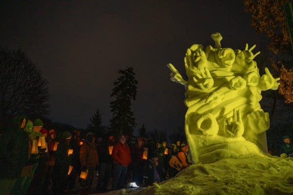 A crowd looks at a snow sculpture of hands reaching out.