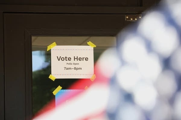 A vote here sign is seen behind a blurry American flag
