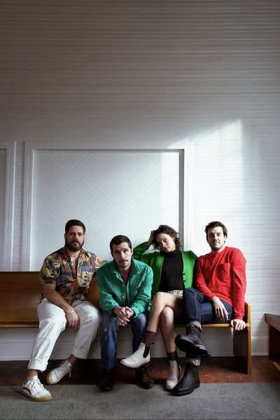 Four people sit together on a wooden bench in a large room