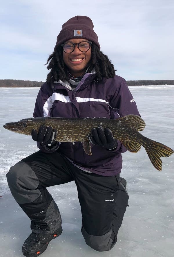 A woman holds a large fish while standing on ice.