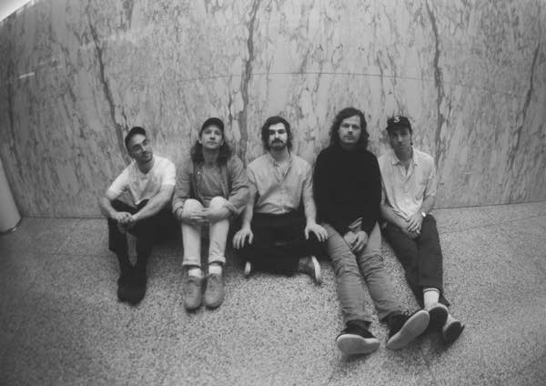 Five men sit in a marble-tiled hallway