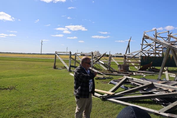 A man points to wooden wreckage in a field.