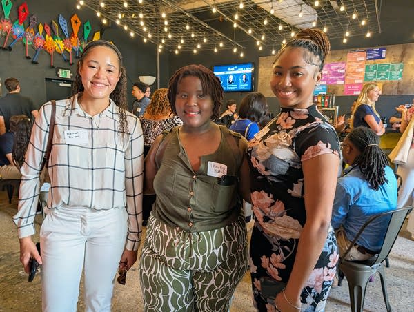 Three young Black woman in work clothes pose for a photo