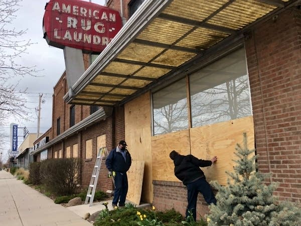 Two people begin to install plywood over windows