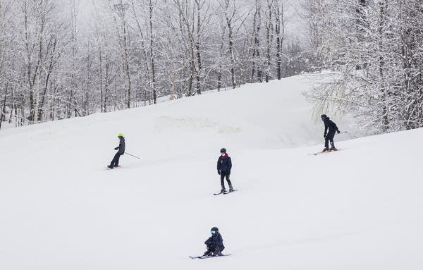 People ski and snowboard down a slope