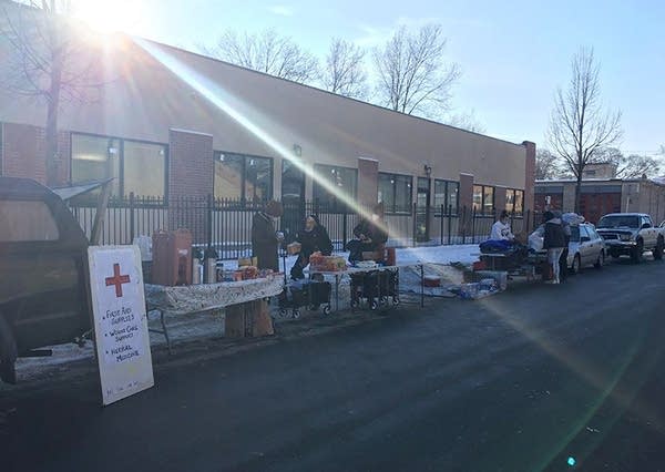 People stand at tables that line a sidewalk. 