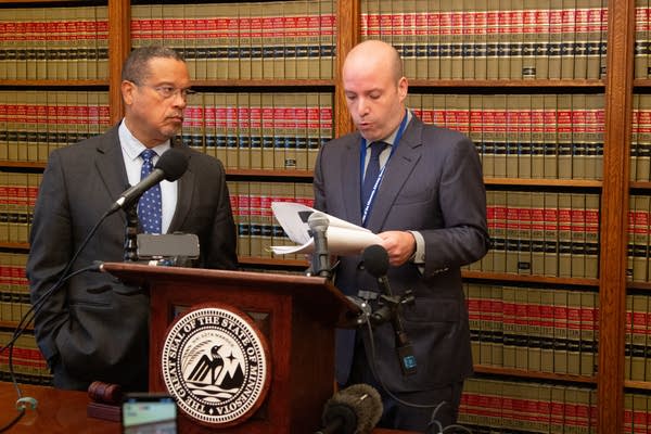 Two men stand behind a podium to speak to press.