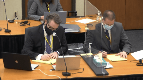 Two men sit behind a desk.