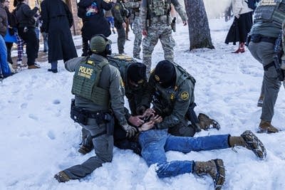 Three Border Patrol agents pin a person to the ground in the snow.
