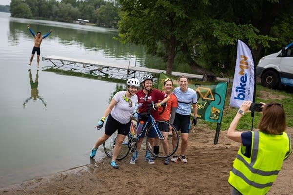 A man jumps off a dock as people pose on a beach