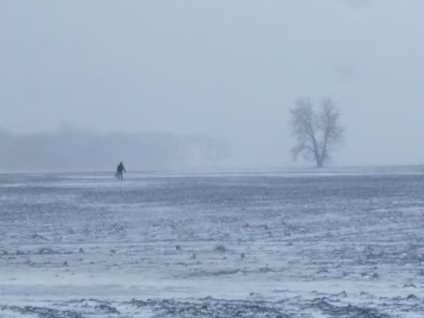 a man walks across a snowy farm field 