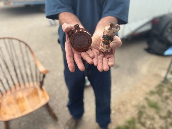 Close-up of a man's hands each holding a miniature pottery liquor bottle.