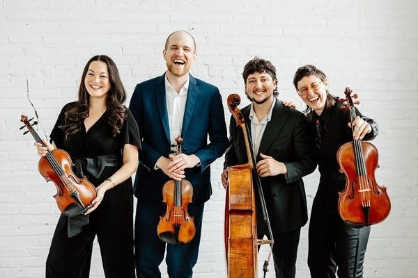 Four people with stringed instruments smile for a group photo