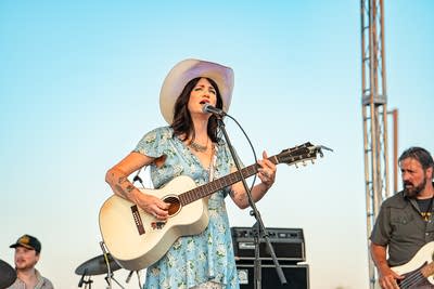 A musician sings and plays guitar on an outdoor stage