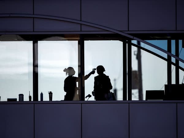 A health-care worker takes the temperature of a visitor