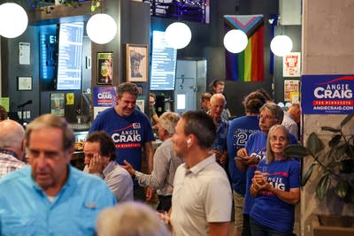 A crowd of supporters wear Angie Craig shirts in a brewery.
