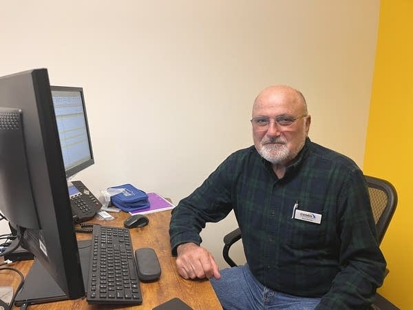 A man sits at a desk behind a computer monitor.