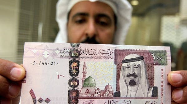 A Saudi banker displays the new one hundred riyal banknote bearing the portrait of Saudi King Abdullah bin Abdul Aziz al-Saud at a bank in Riyadh